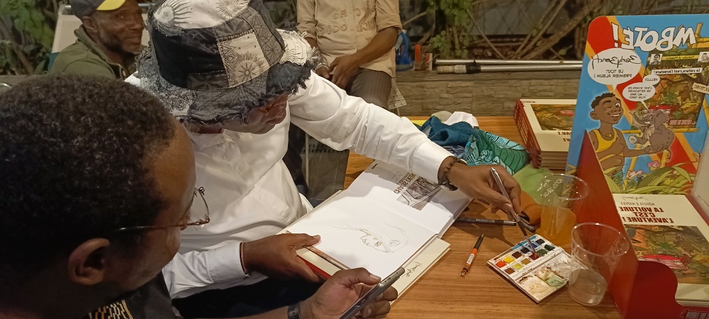 1 : Barly Baruti fait une dédicace à l’aquarelle au Memling / Adiac
