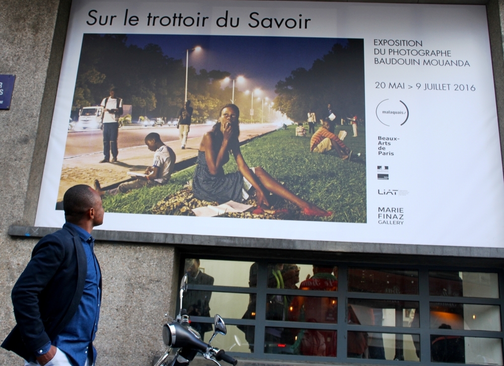 Baudoin Mouanda admirant le panneau géant de l'annonce de l'exposition "Sur le trottoir du savoir" à Paris