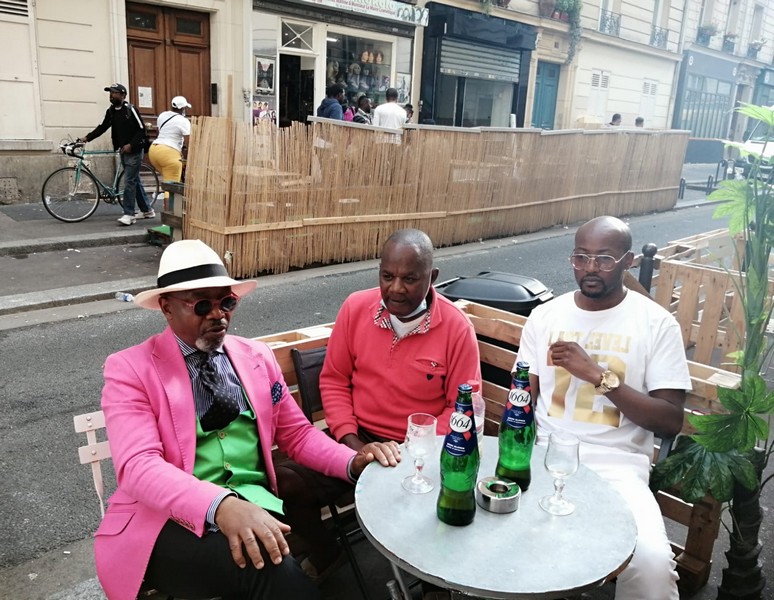 J.A. Le Bachelor au premier plan sur la photo en partant de gauche à droite, et le Parisien Lasiambo et de Negus, styliste, attablés sur une terrasse à Paris, Château Rouge 
